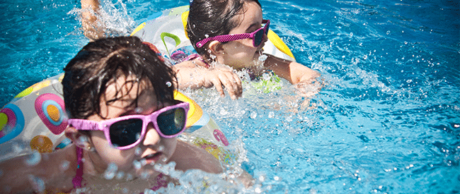 Two children wearing sunglasses splash in a pool with brightly coloured, round pool floats
