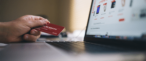 Close up of a laptop showing a shopping list on the screen with a hand holding a credit card