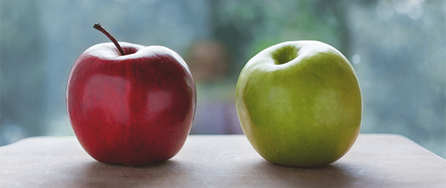 Two apples of a similar size sit on a table, one is a red spartan, the other is a green delicious