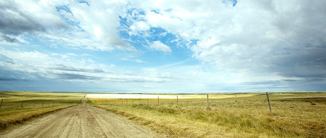 Prairie scene with a cloudy sky, empty grass fields, and a straight dirt road